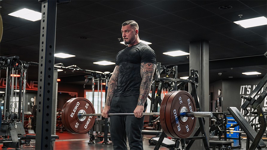 En mand i et fitnessmilj� udf�rer d�dl�ft med en v�gtstang.